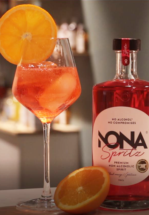Verre de Spritz sans alcool accompagné d’une bouteille de Nona Spritz, cocktail frais et pétillant.
